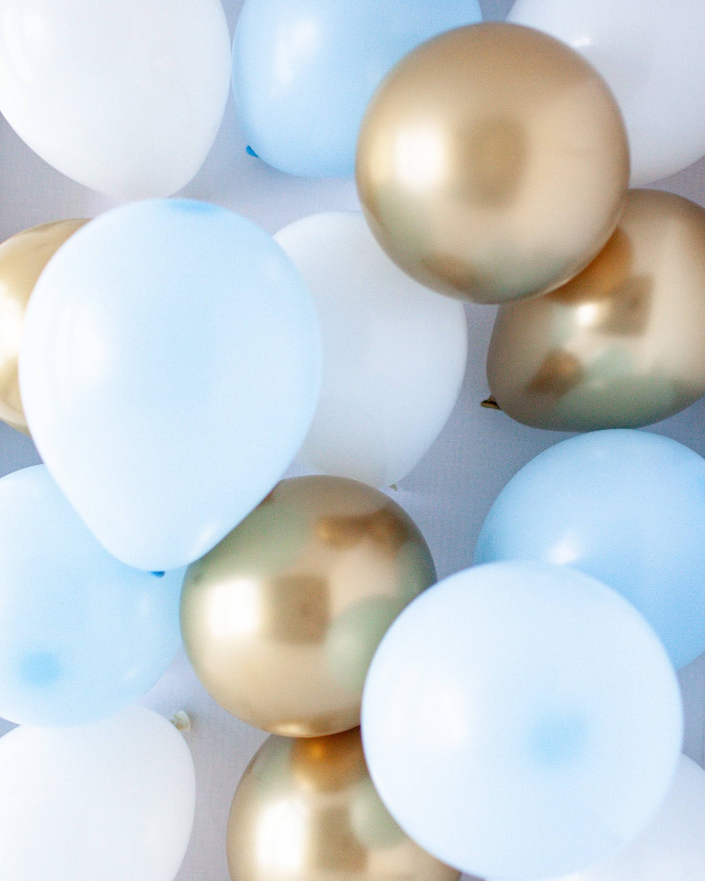 A vibrant mix of blue, white, and gold balloons, featuring glossy and matte finishes, creating a festive atmosphere.