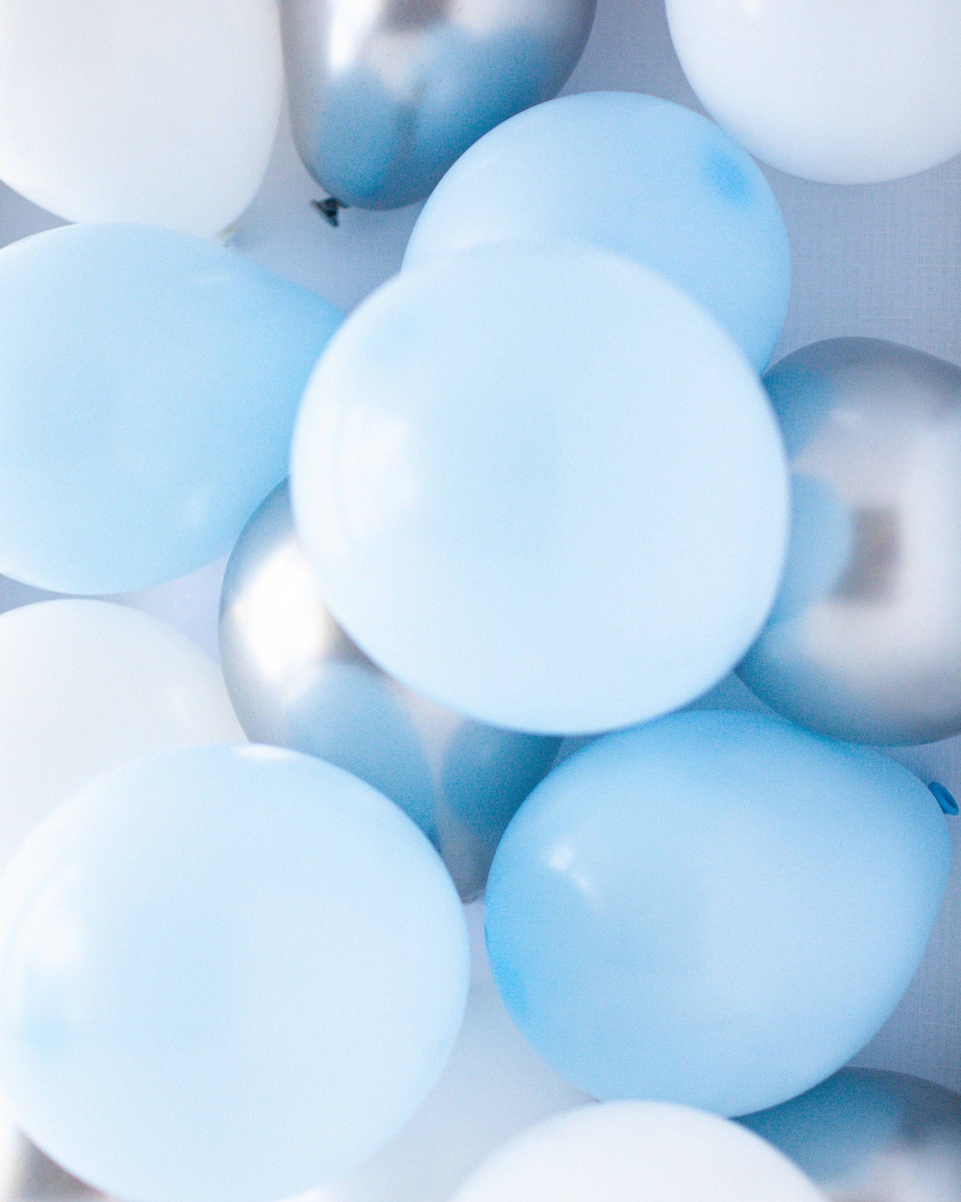 A mix of light blue, white, and silver balloons layered together, creating a festive and vibrant display.