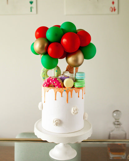 A festive cake topped with colorful balloons and vibrant sweets, showcasing a playful holiday theme.