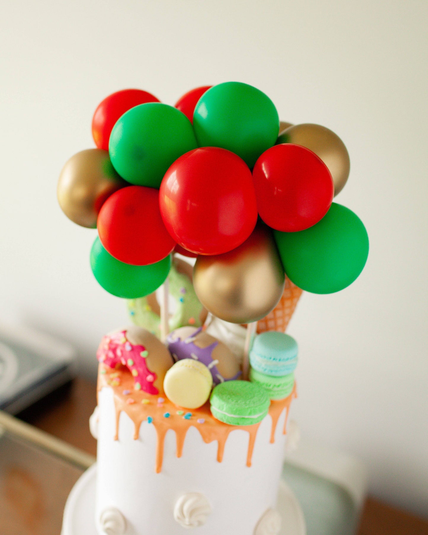 A festive cake topped with colorful balloons, sprinkles, and playful decorations in vibrant red, green, and gold hues.