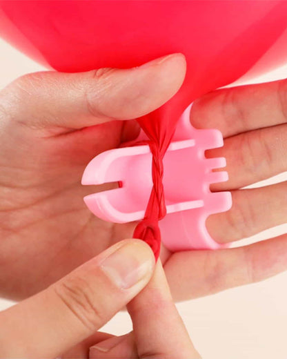 A close-up of a hand tying a red balloon knot using a pink knotting tool, demonstrating the twisting technique.