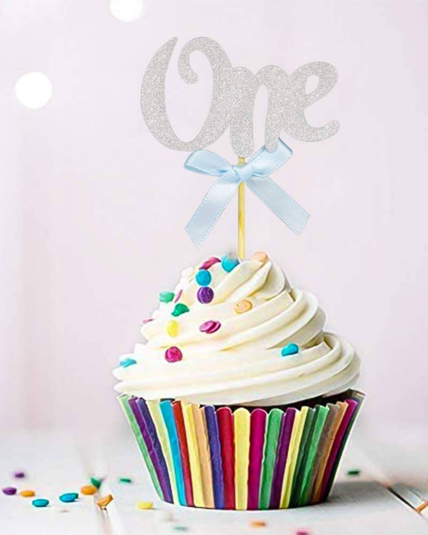 A colorful cupcake topped with swirls of frosting, featuring a glittery "One" and a blue ribbon bow.