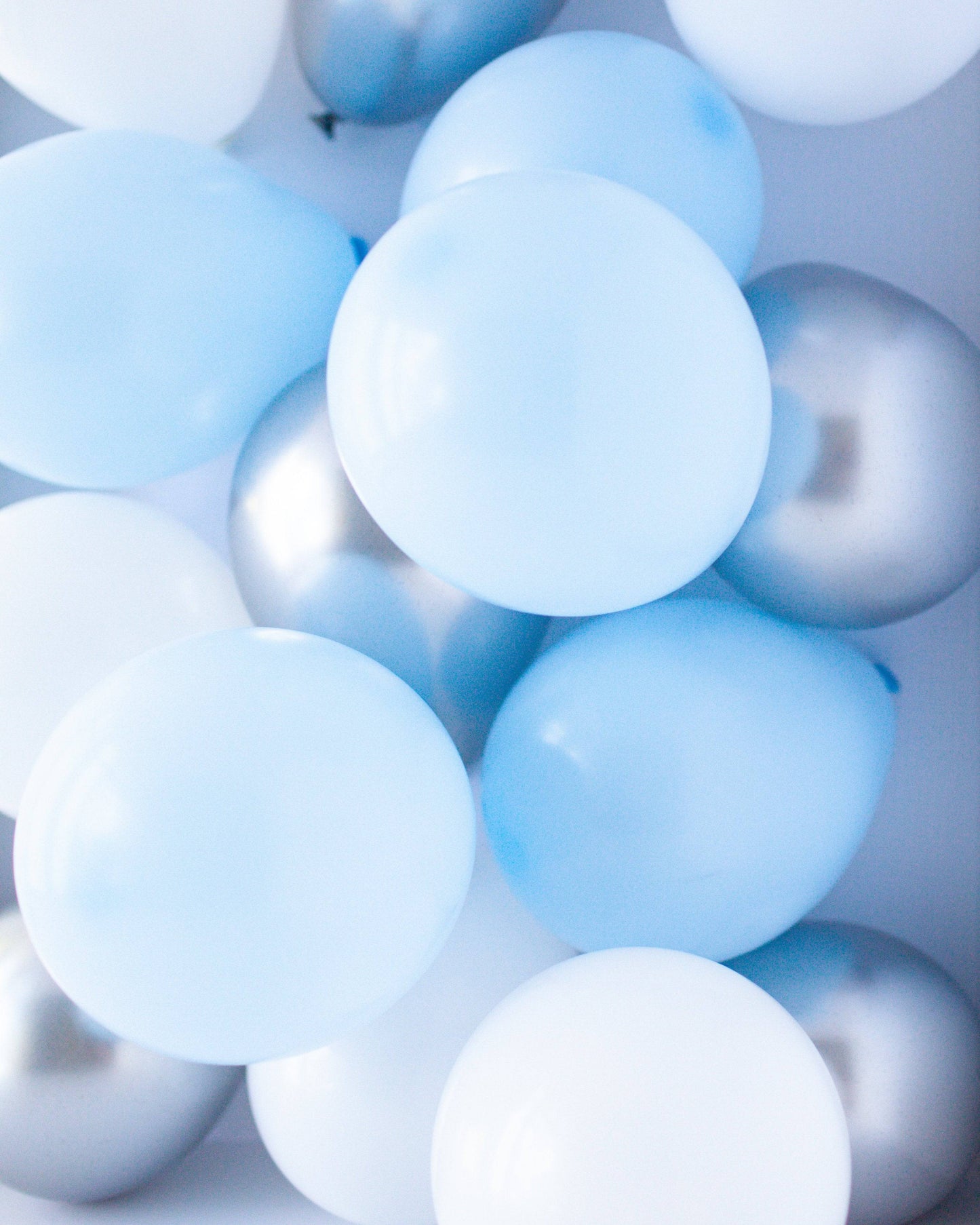 A colorful mix of light blue, white, and silver balloons, creating a festive and cheerful atmosphere.