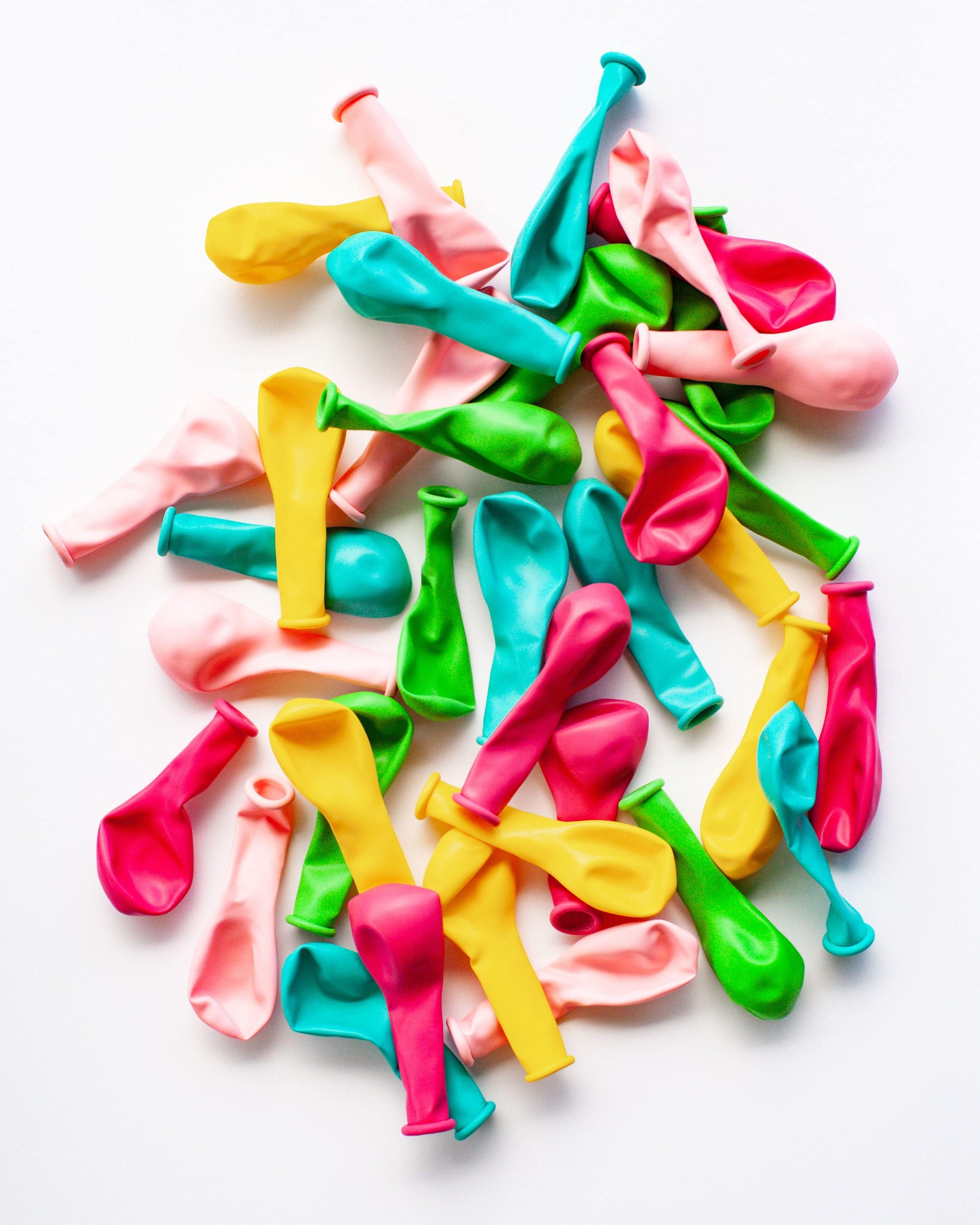 A vibrant mix of mini balloons in pink, yellow, green, and blue scattered on a white background.