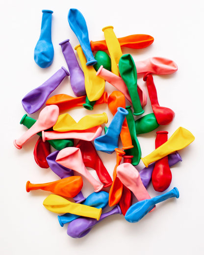 A colorful assortment of mini balloons in various shades, scattered on a light background.