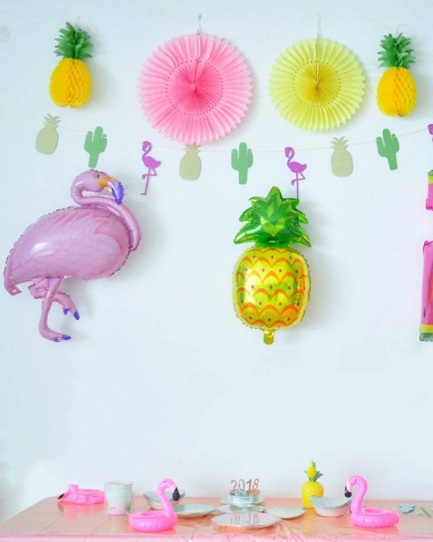 Colorful flamingo and pineapple balloons decorate a festive table setting with pink accents and playful cactus cutouts.