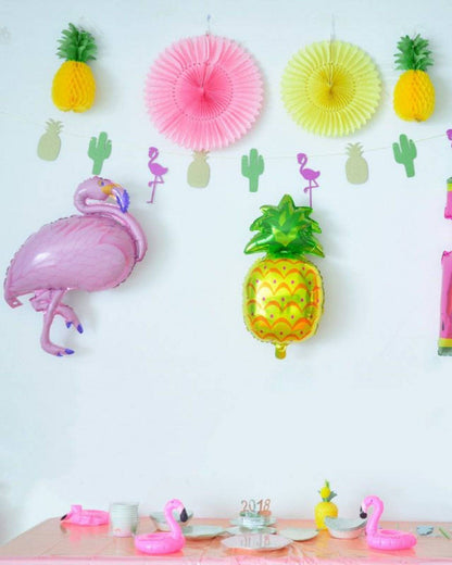 Colorful flamingo and pineapple balloons decorate a festive table setting with pink accents and playful cactus cutouts.