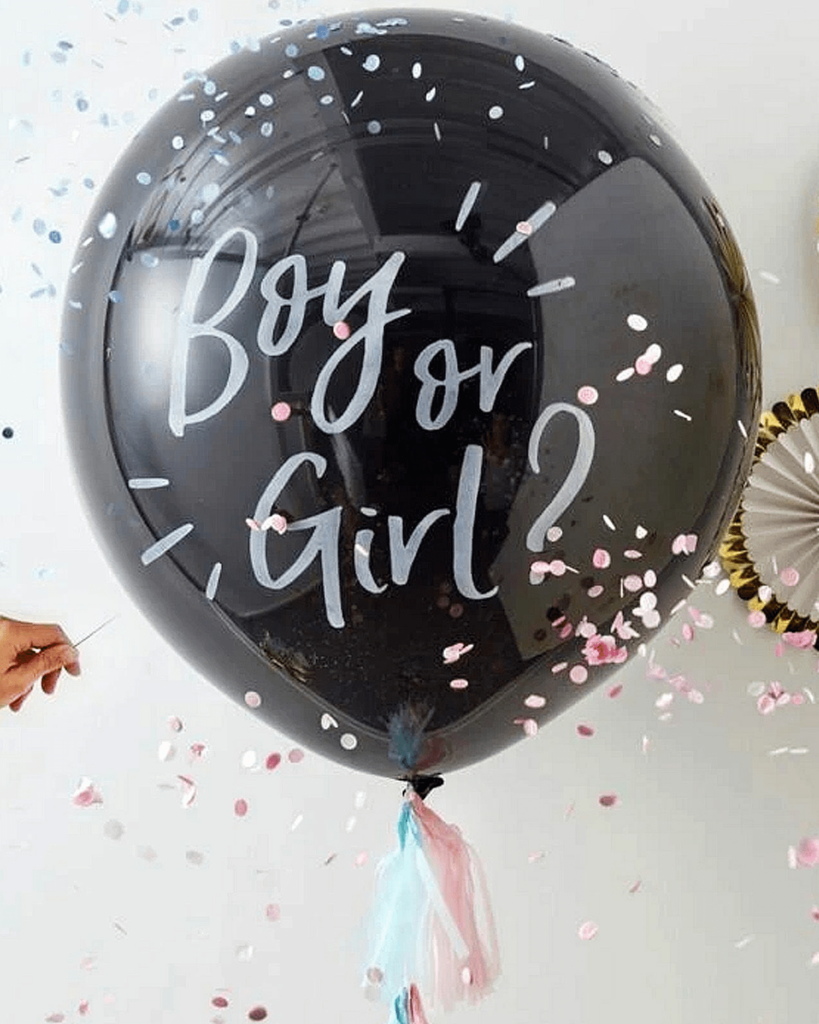 Black balloon with "Boy or Girl?" in white script, surrounded by pink and blue confetti, held by a hand.