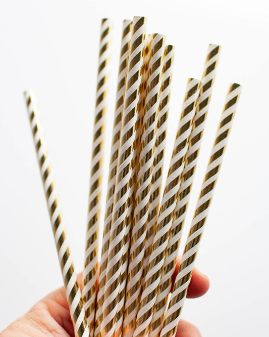 A hand holds multiple gold and white striped straws against a plain background.