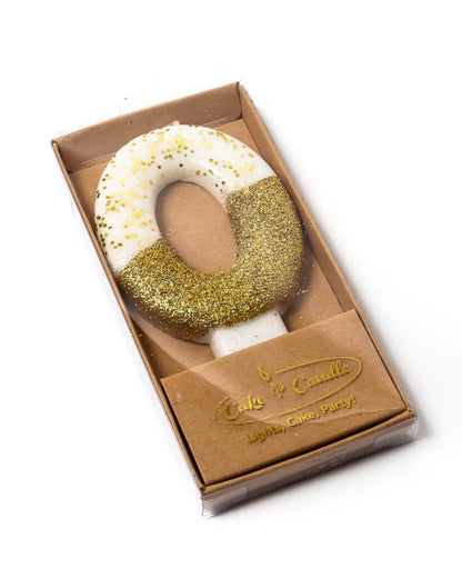 Gold glitter-dipped candle in the shape of the number 0, presented in a clear box with a brown base.