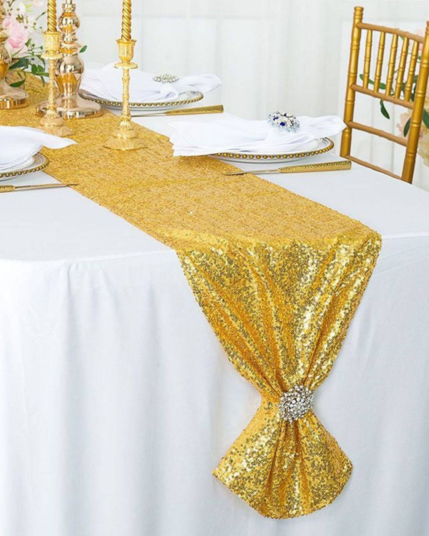 A shimmering gold sequin table runner drapes elegantly over a white tablecloth, adorned with golden candlesticks and plates.