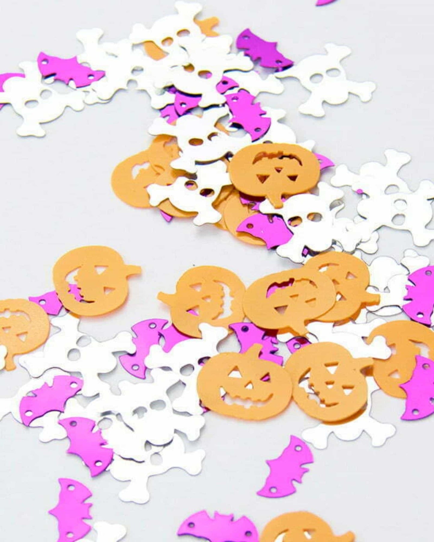 Colorful confetti featuring bats, skulls, and jack-o'-lanterns in orange, white, and pink scattered on a light surface.