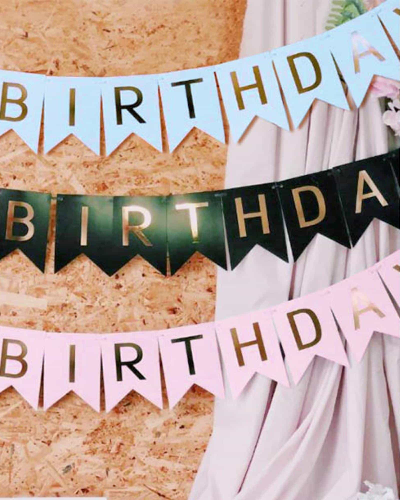 Colorful "Birthday" banners in light pink, blue, and black, adorned with shiny gold lettering against a textured backdrop.