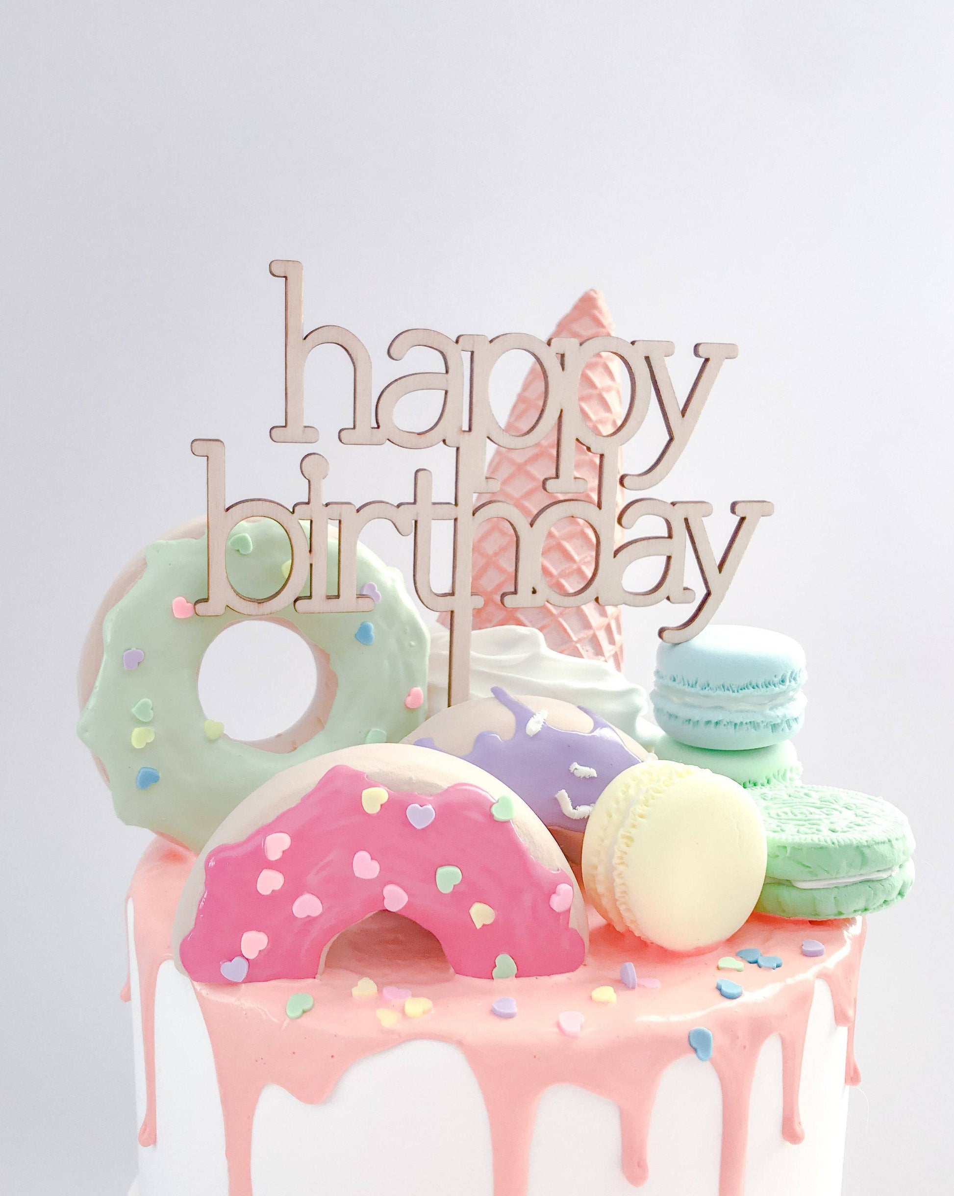 Colorful birthday cake topper featuring playful sweets and a "happy birthday" sign in elegant cursive.