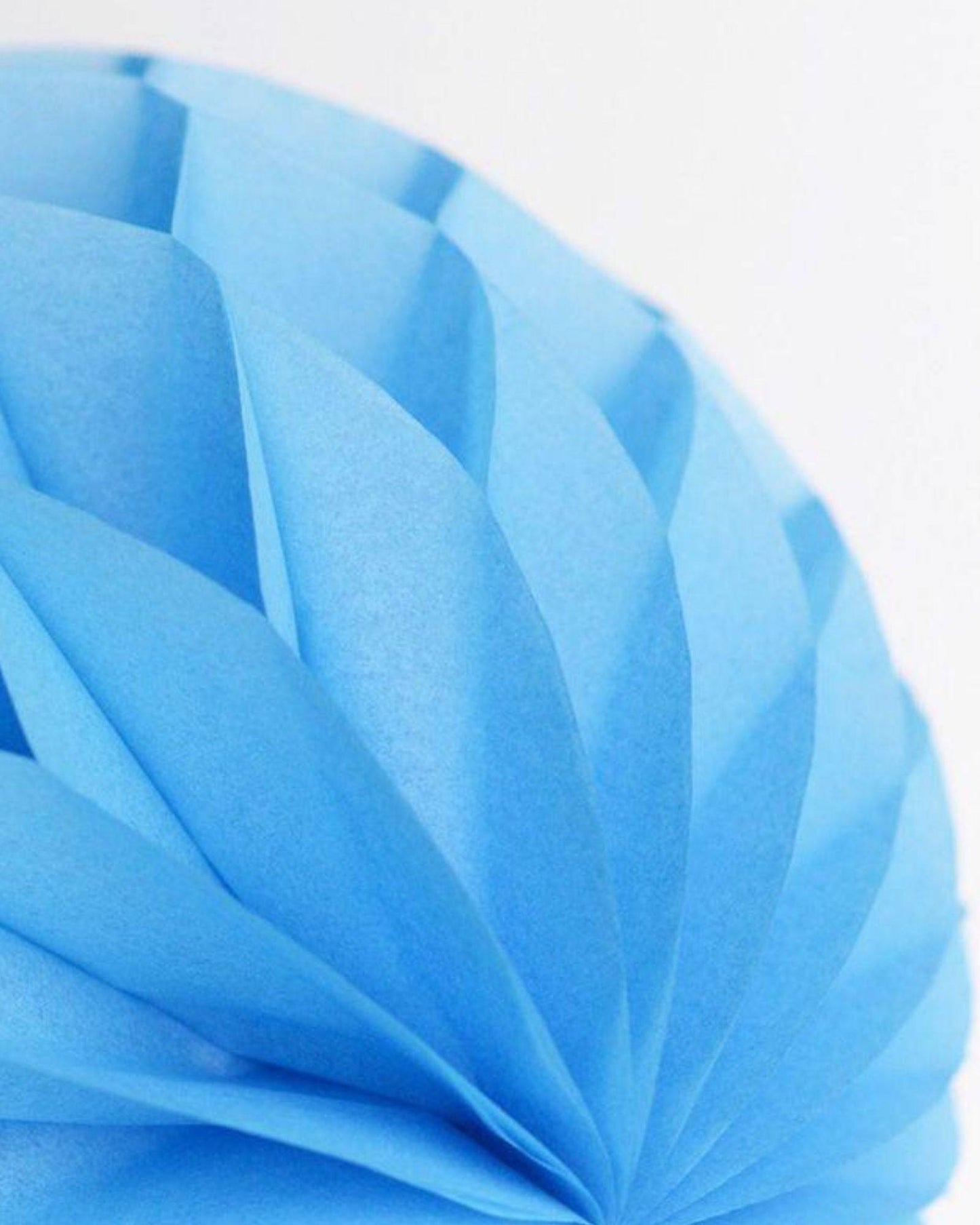 A round decoration made of layered light blue paper, showcasing a delicate fan-like texture against a white background.