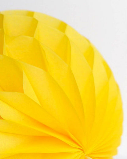 A vibrant yellow spherical decoration with intricate pleats, creating a dynamic, sunny appearance against a light background.