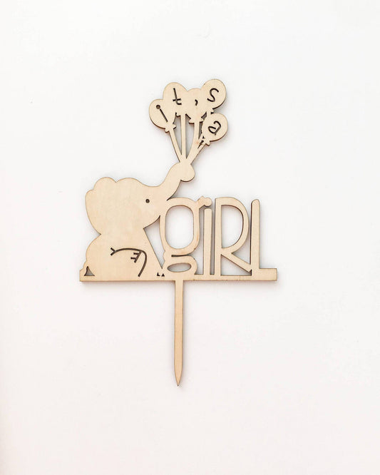 Wooden cake topper featuring a playful elephant holding balloons with the text "it's a girl" in a whimsical font.