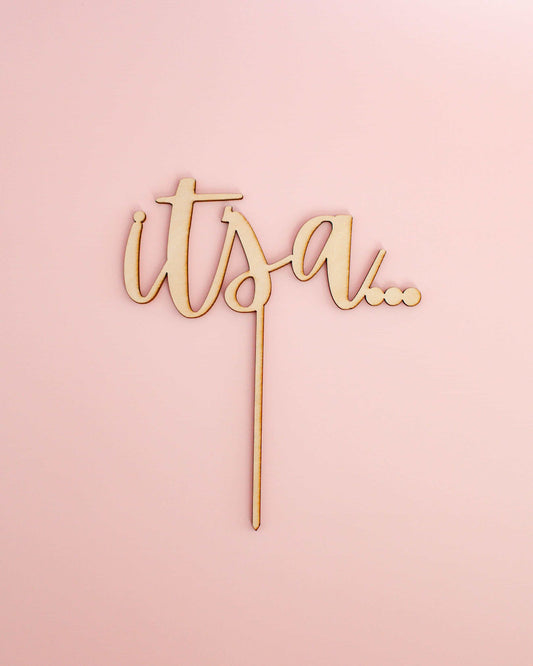 Wooden topper featuring playful script saying "it's a..." against a soft pink background.