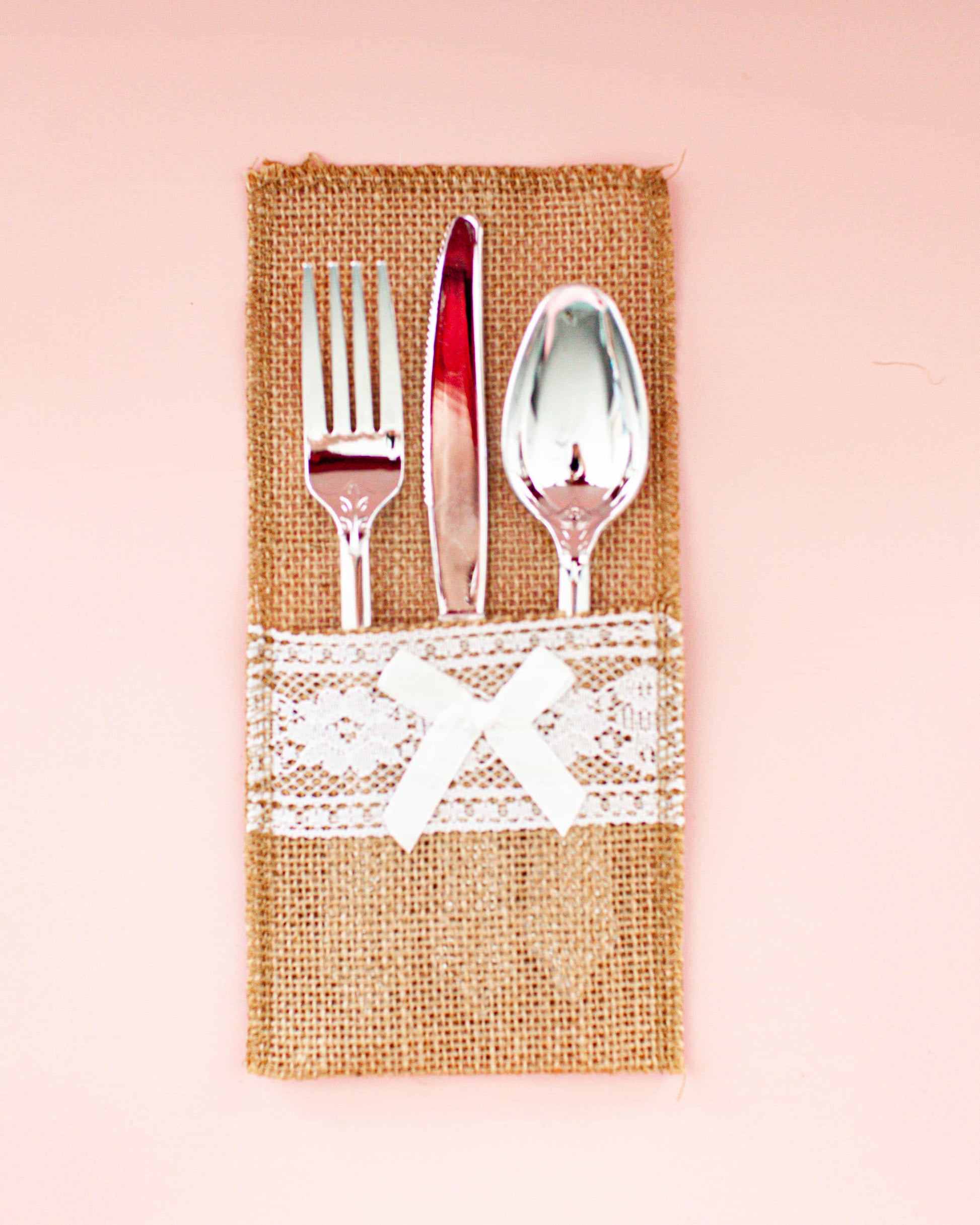 A rustic burlap wrap holds a fork, knife, and spoon, adorned with a delicate lace band and bow.