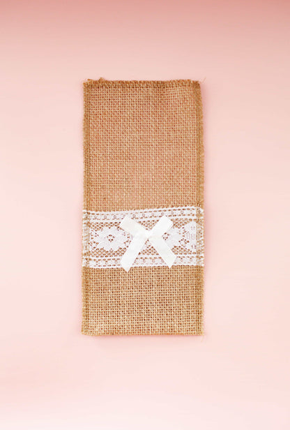 A rustic burlap wrap adorned with delicate lace and a satin bow, set against a soft pink background.