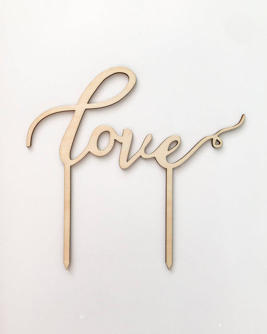 Elegant wooden cake topper with the word "love" in a flowing script, set against a light background.