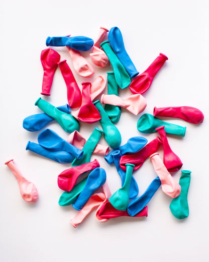 Colorful mini balloons in pink, blue, and green scattered on a white background, creating a playful and vibrant scene.