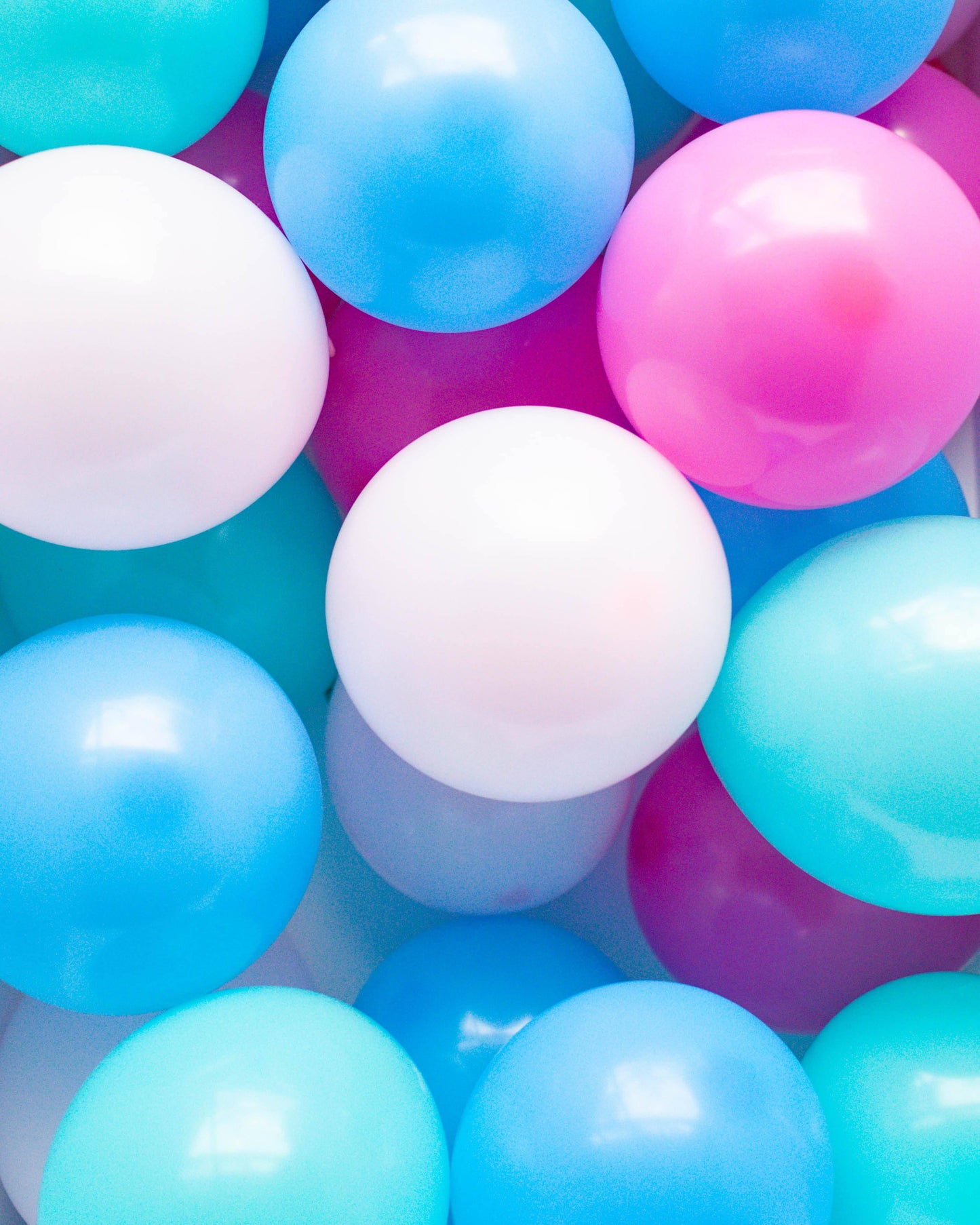 Colorful assortment of glossy, round balloons in shades of pink, blue, and white, creating a playful and vibrant scene.