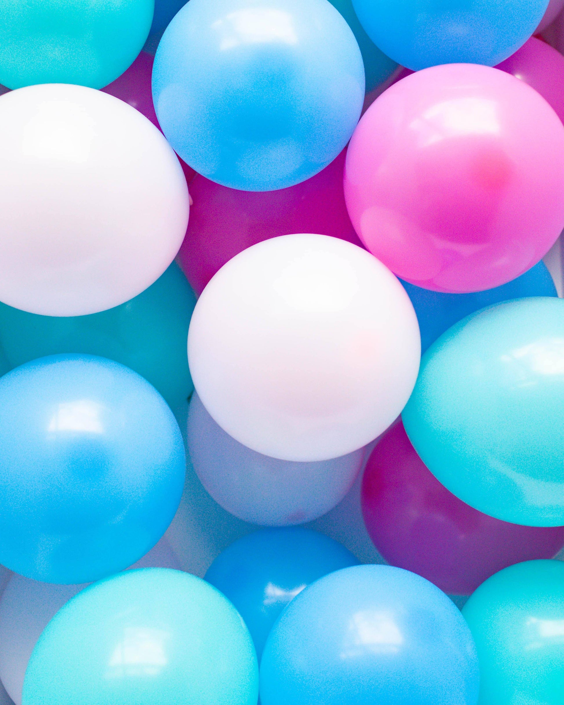 Colorful assortment of glossy, round balloons in shades of pink, blue, and white, creating a playful and vibrant scene.