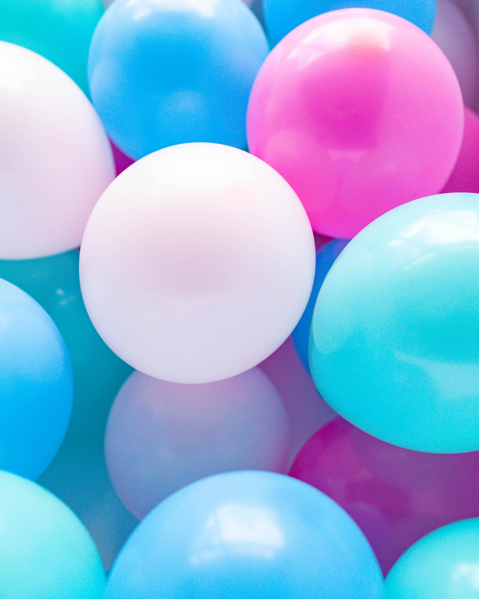 A colorful assortment of glossy balloons in shades of pink, white, and blue clustered together.