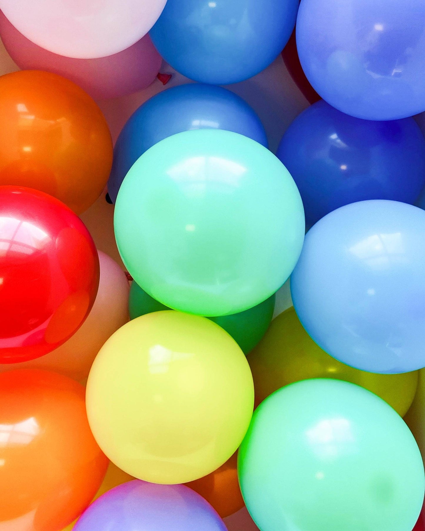 A vibrant mix of glossy balloons in various colors, including red, orange, green, blue, and purple, clustered together.