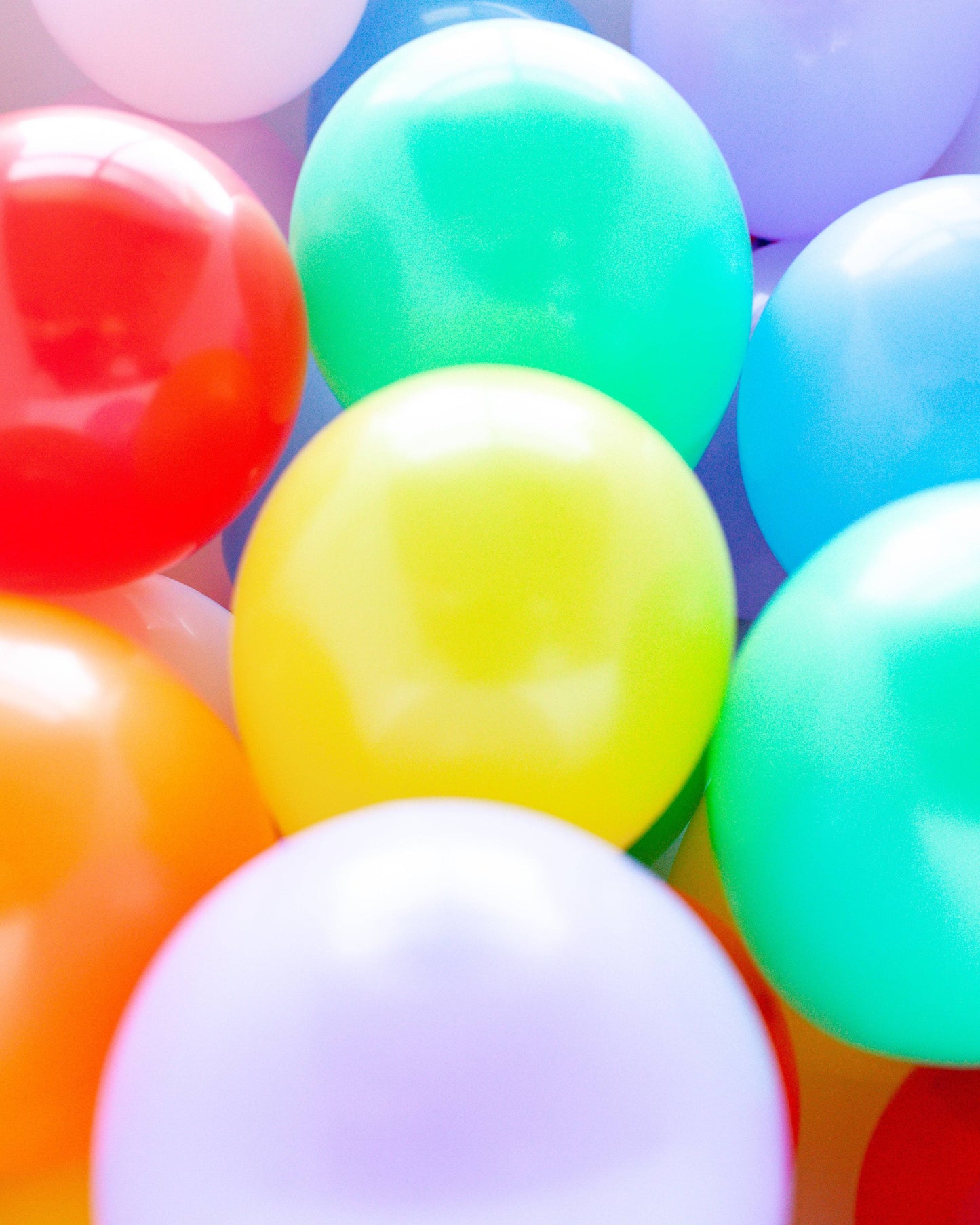 A colorful assortment of round balloons in vibrant shades of red, yellow, green, blue, and purple, arranged closely together.