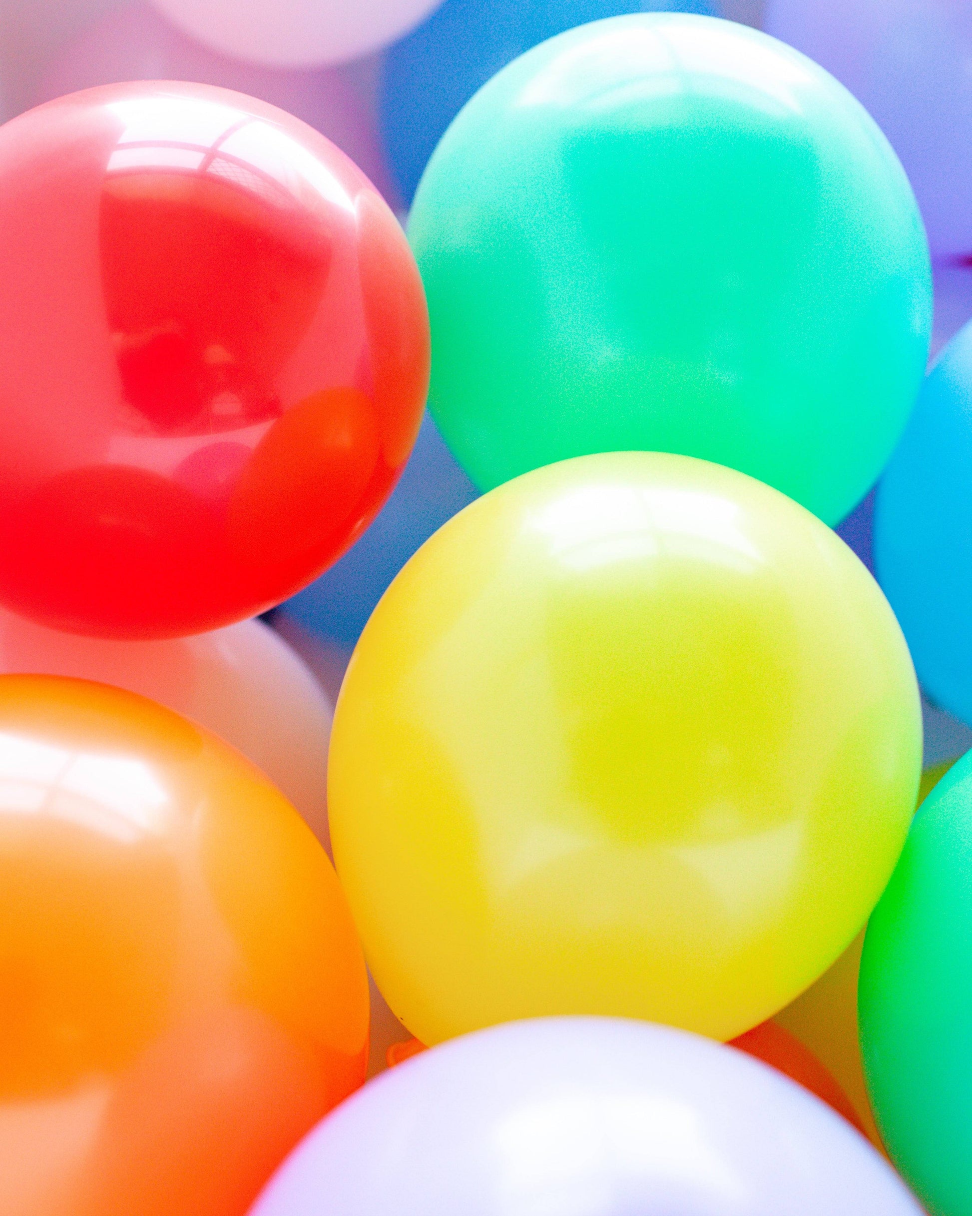 Colorful balloons in various shades including red, yellow, green, and orange, clustered together against a soft background.