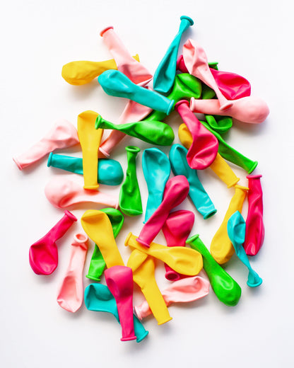 A vibrant mix of pastel and bright balloons in various shapes scattered on a white background.