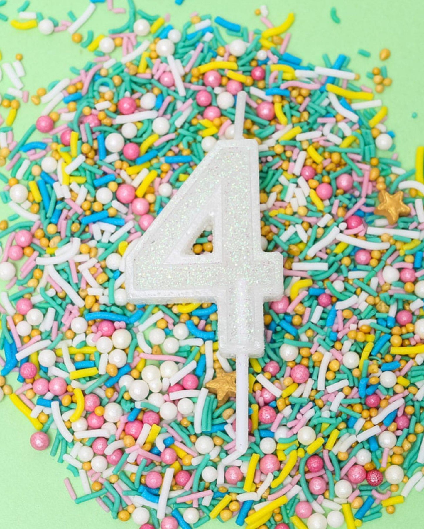 A glittery white number 4 candle surrounded by colorful sprinkles on a light green background.