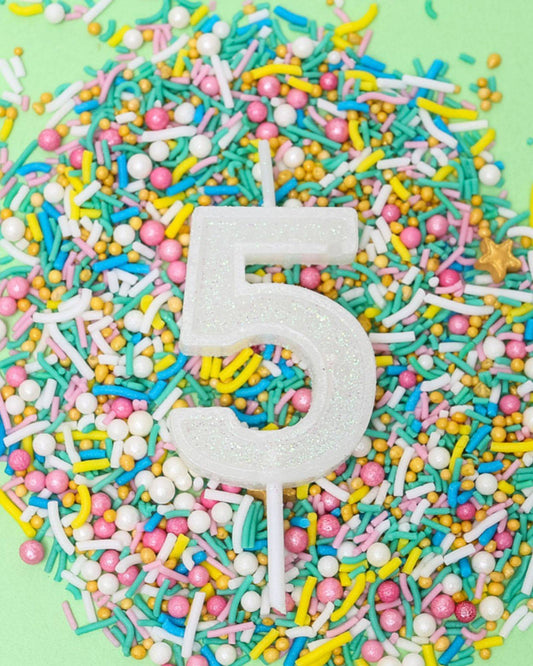 A glittery white number 5 candle surrounded by colorful sprinkles on a mint green background.