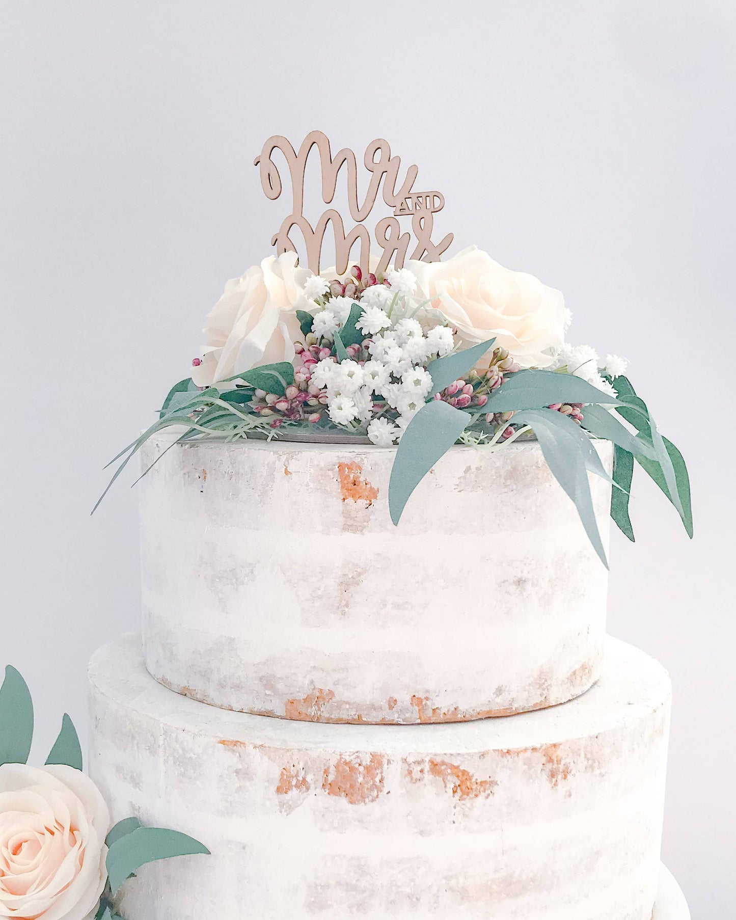 A tiered cake adorned with soft roses, greenery, and a wooden "Mr and Mrs" topper.