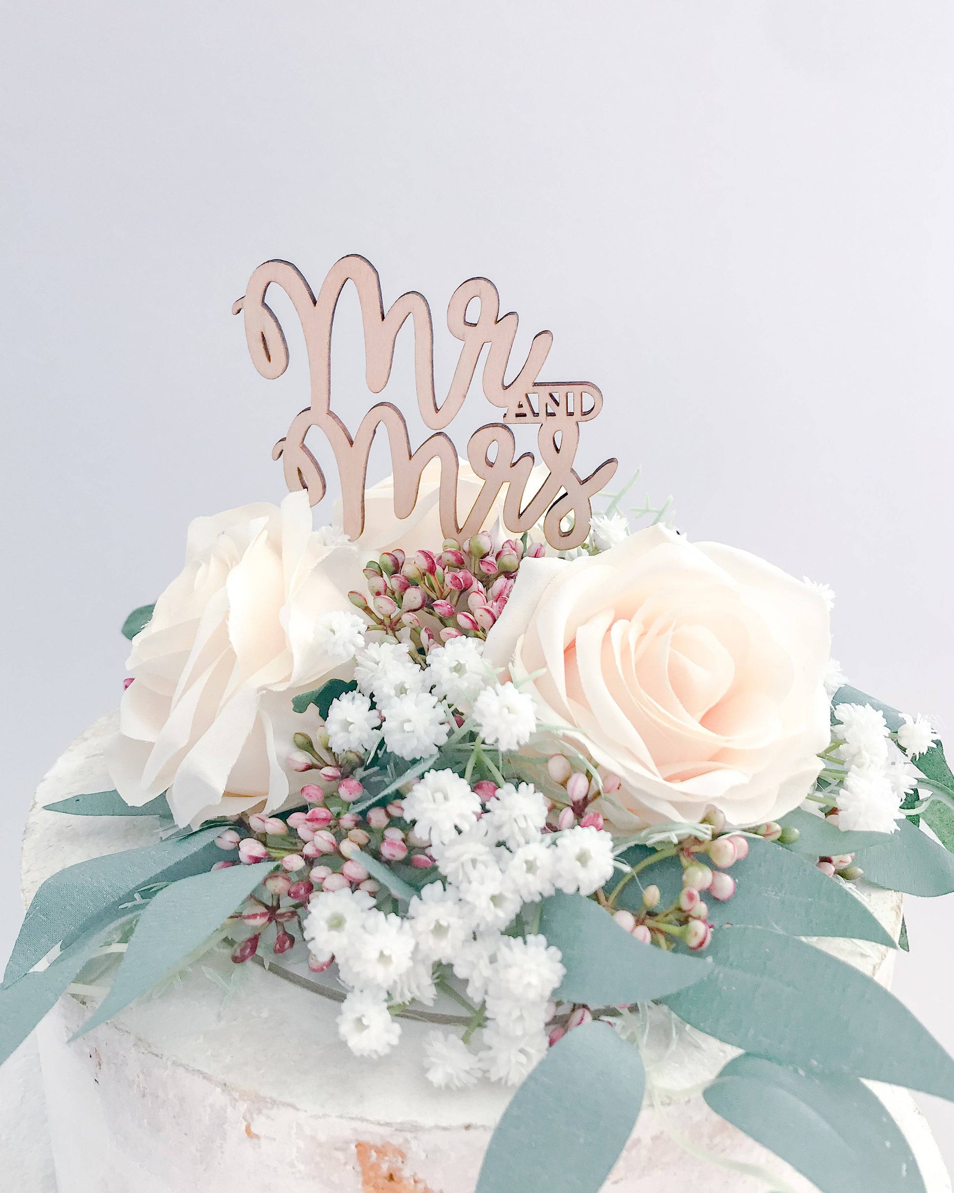 Elegant wooden "Mr. and Mrs." topper surrounded by soft pastel roses and delicate greenery. Perfect for celebrations.