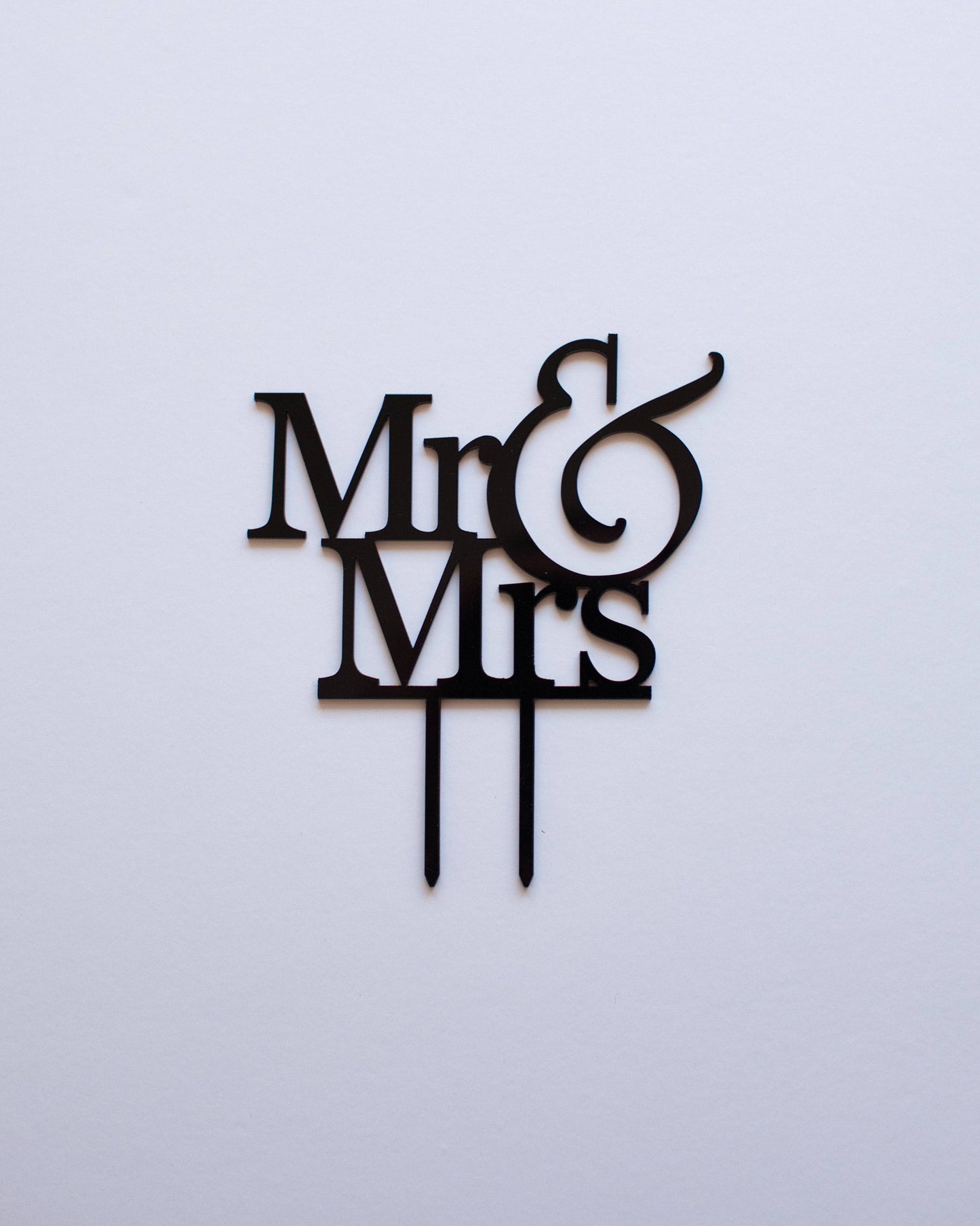 Black "Mr & Mrs" topper with elegant lettering and two support prongs against a light backdrop.