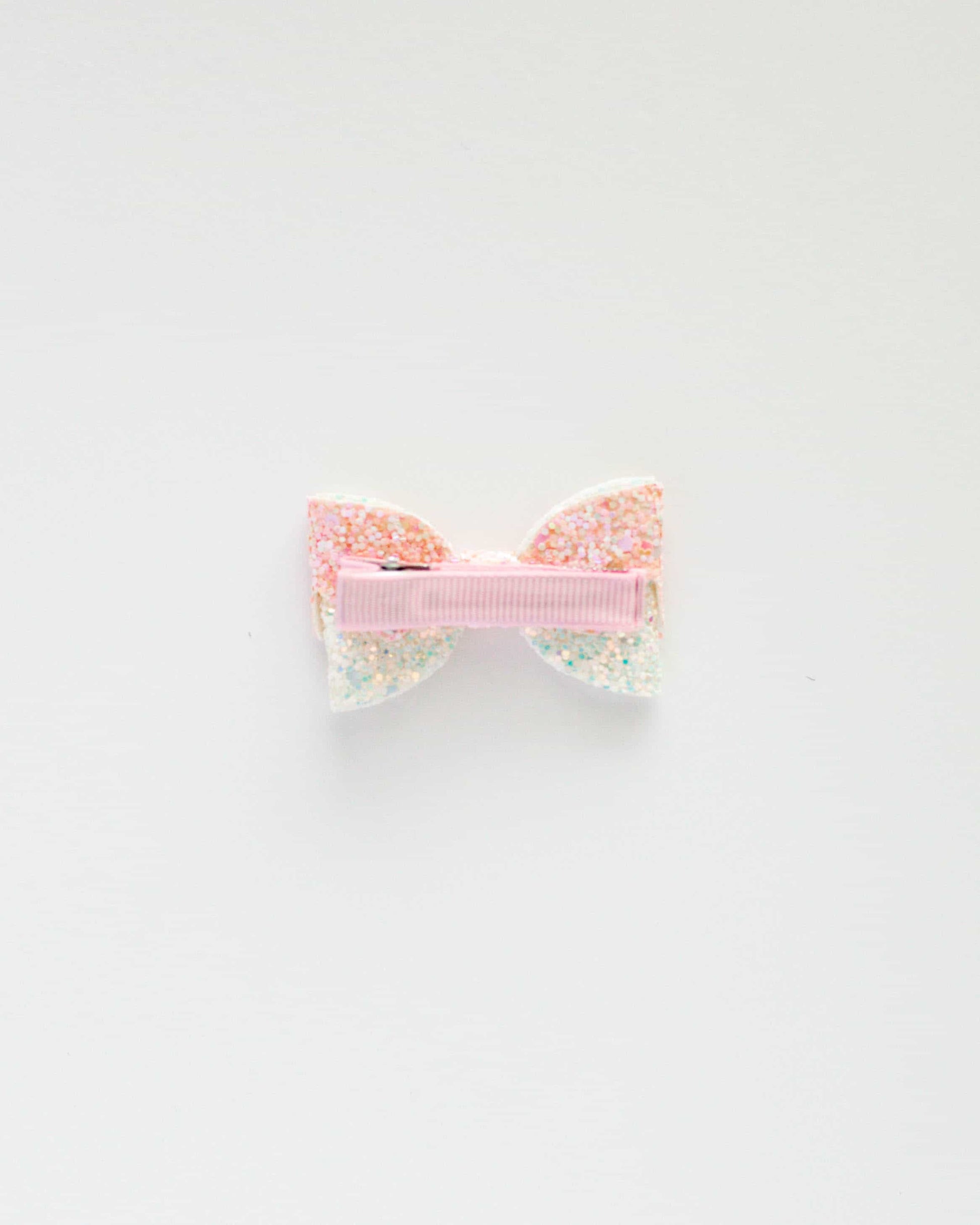 Glittery pastel bow clip with a pink ribbon center, set against a clean white background.