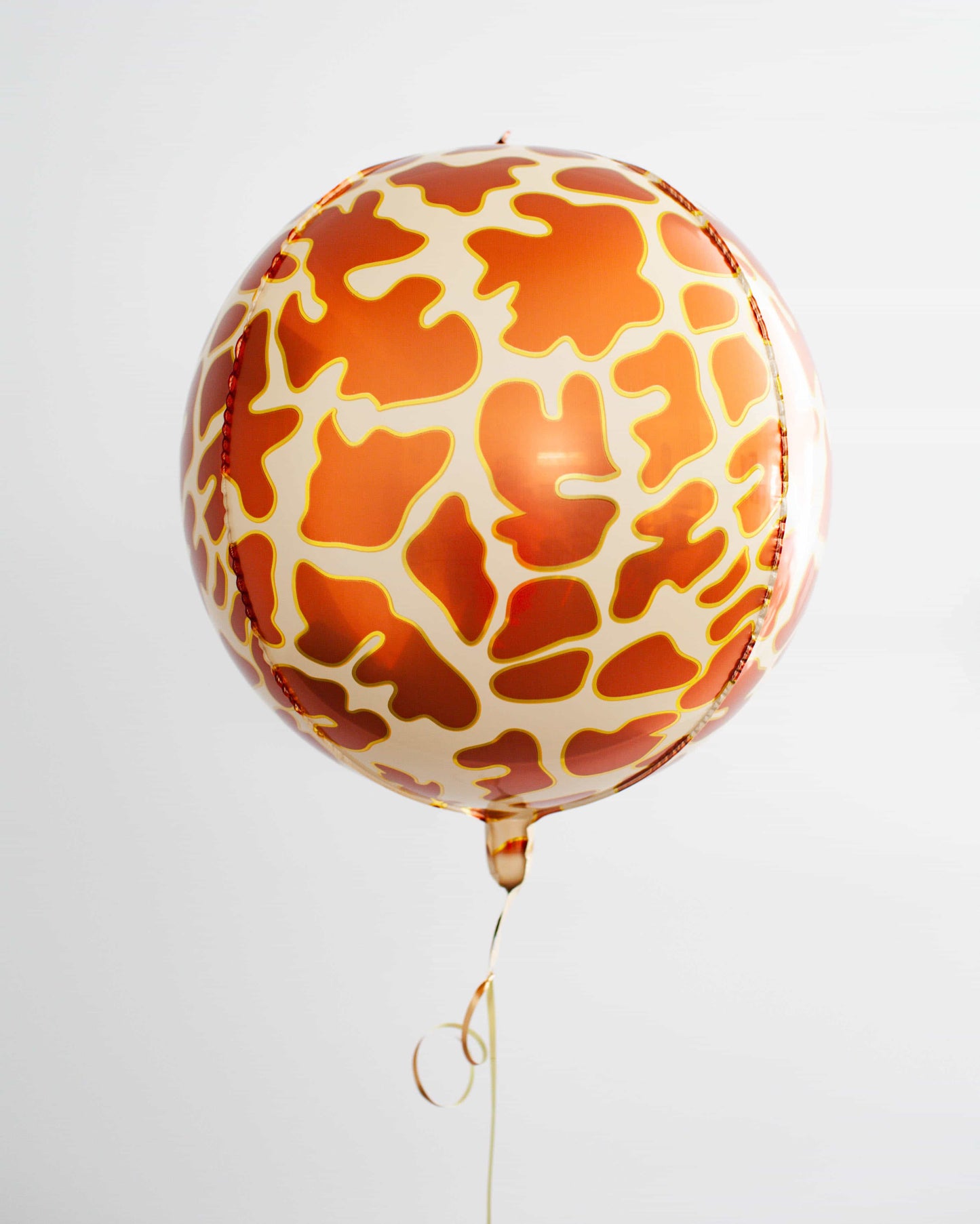 Round balloon featuring a vibrant orange and cream giraffe print, suspended by a golden ribbon against a light background.