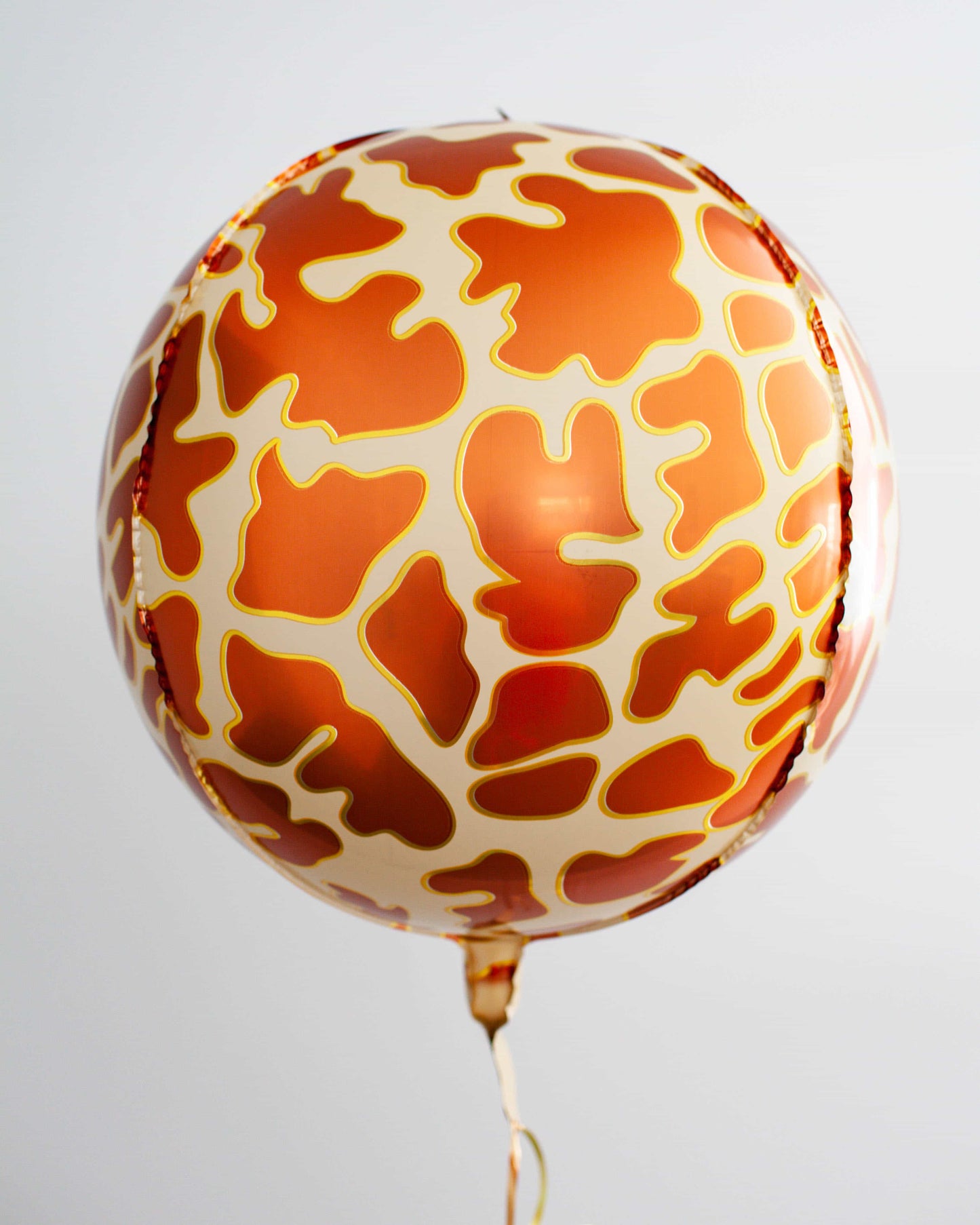 A round, glossy balloon featuring a vibrant orange and cream giraffe pattern, suspended by a golden string.