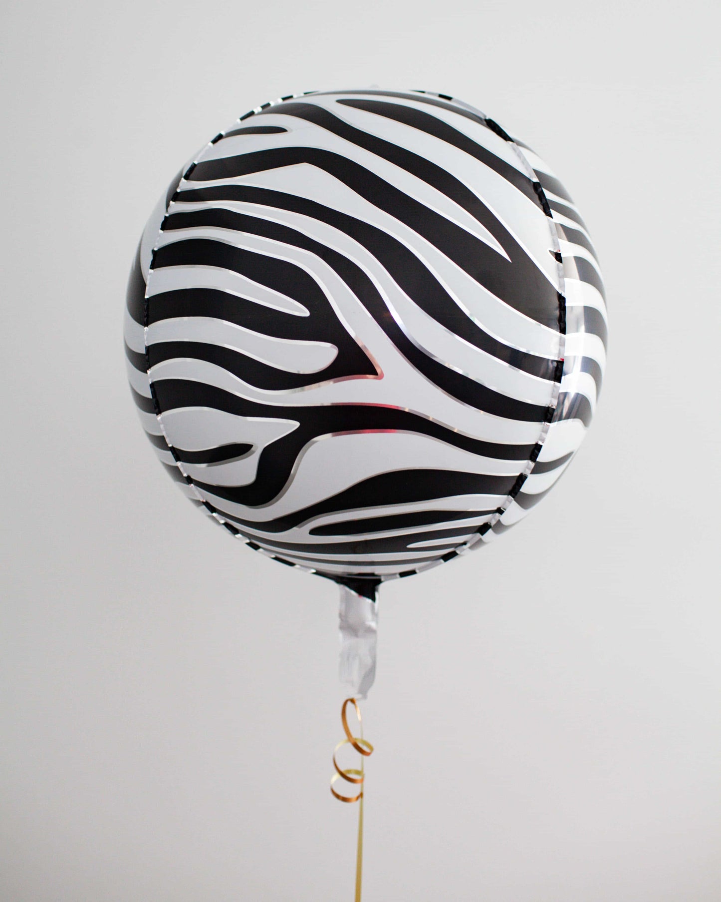 A black and white striped balloon floats elegantly, tied with a golden ribbon against a light background.