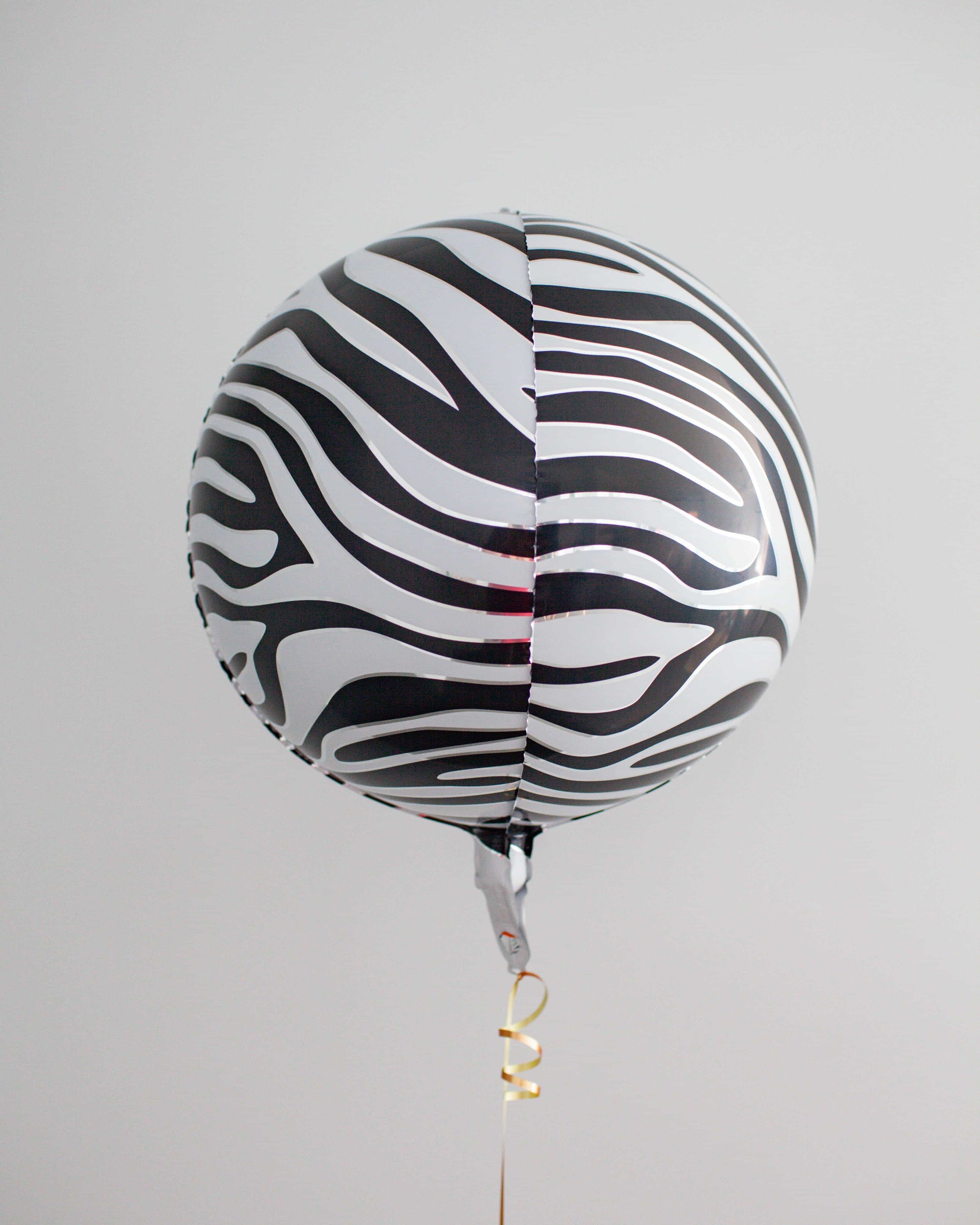 Black and white striped round balloon with a shiny surface, floating against a light gray background.