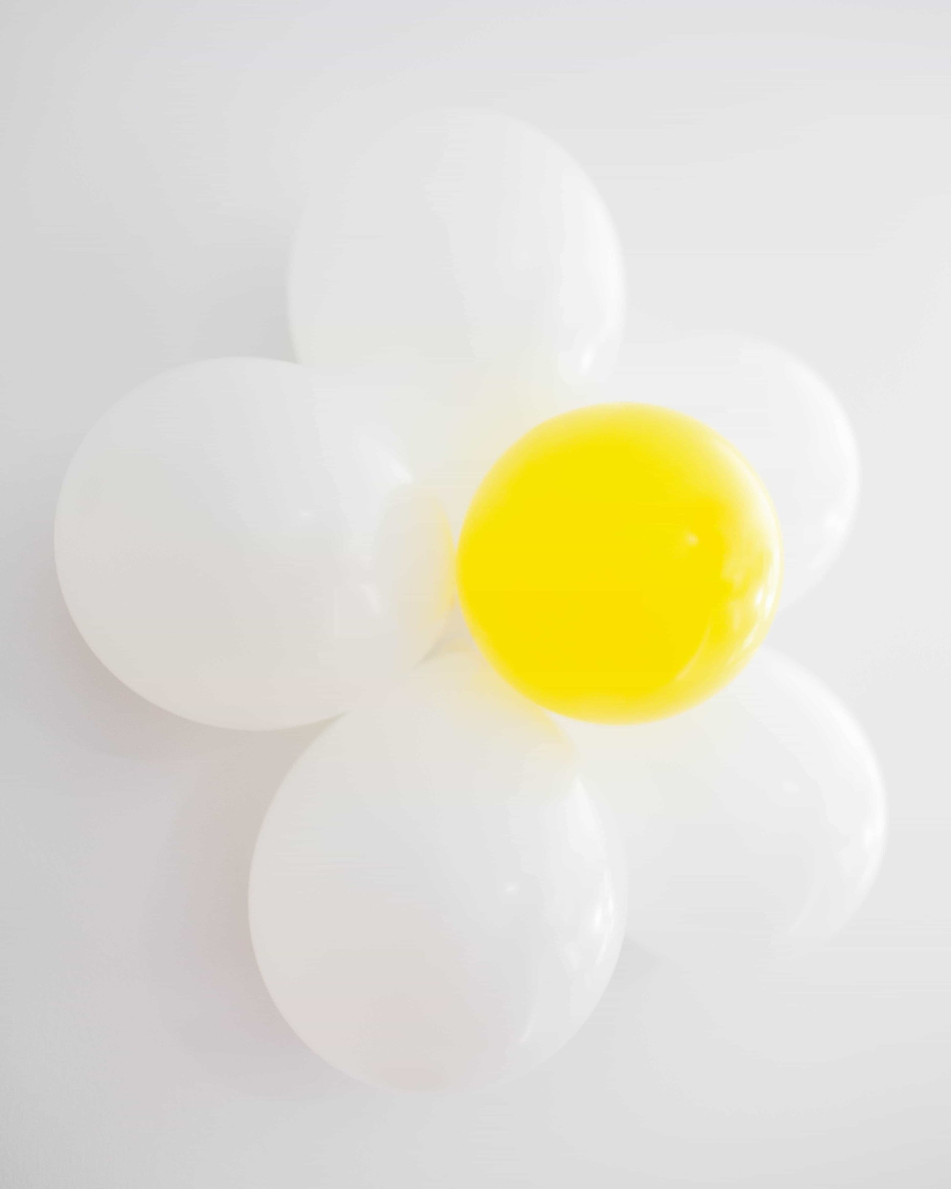 A cluster of white and yellow balloons arranged to resemble a flower against a light background.