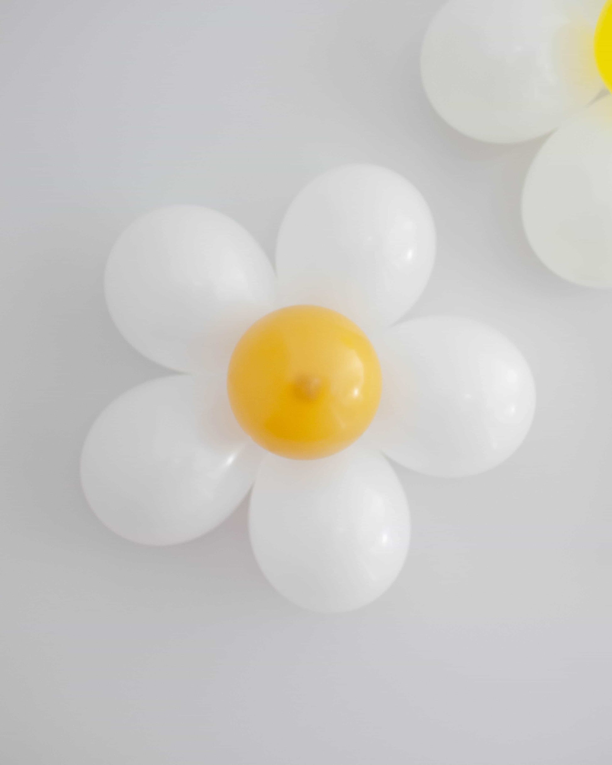 A playful flower shape with white petals and a bright yellow center, set against a soft, light background.