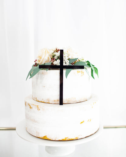 A two-tiered white creation adorned with soft roses, greenery, and a sleek black ribbon, set against a bright backdrop.