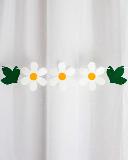 A string of white daisies with yellow centers and green leaves against a light backdrop.