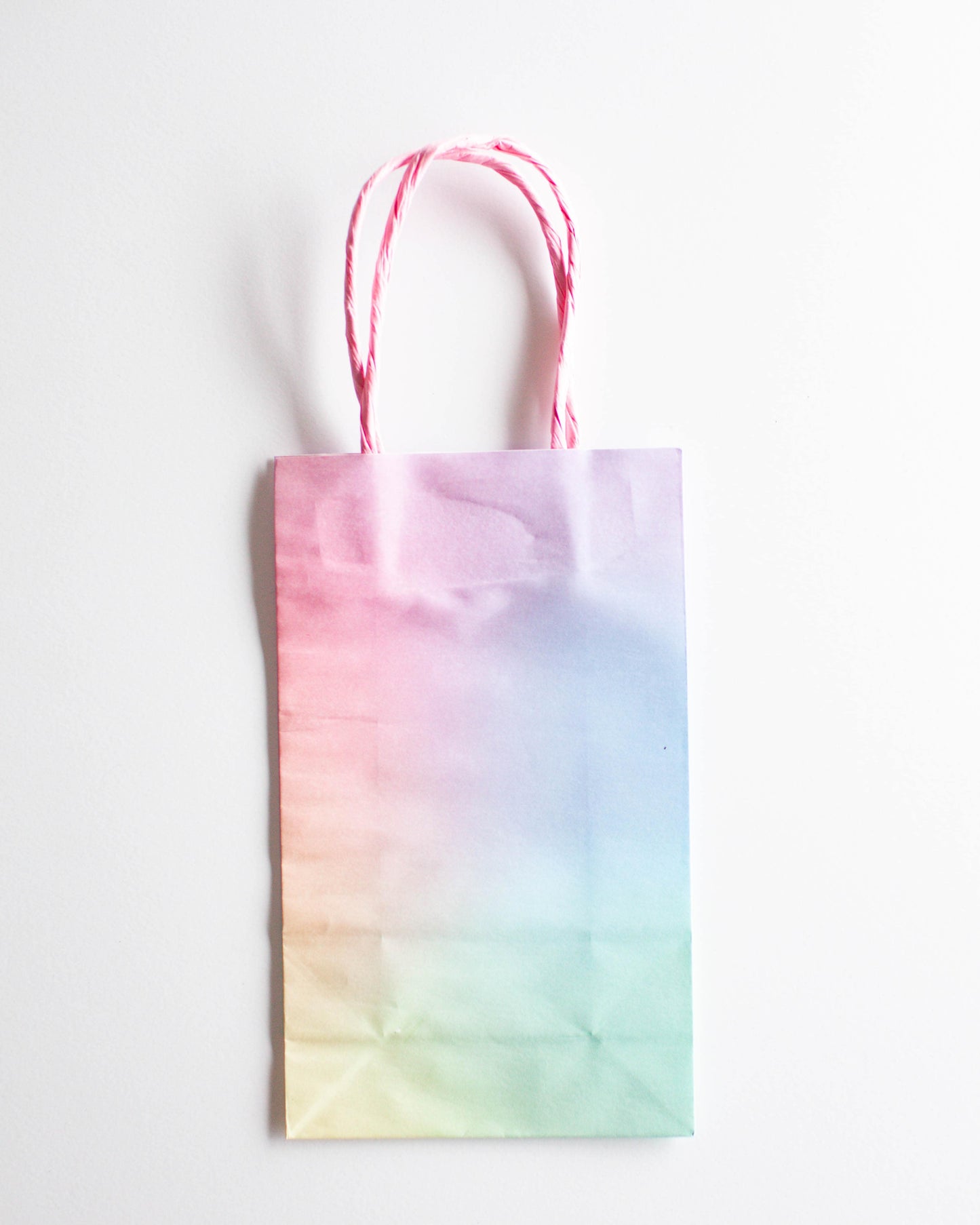 A pastel gradient bag with pink twisted handles, featuring soft hues of pink, blue, and green.