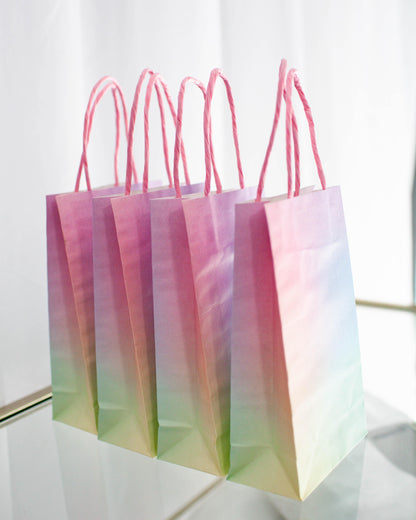 Five pastel gradient bags with pink handles arranged in a row, showcasing soft hues of pink, purple, and green.