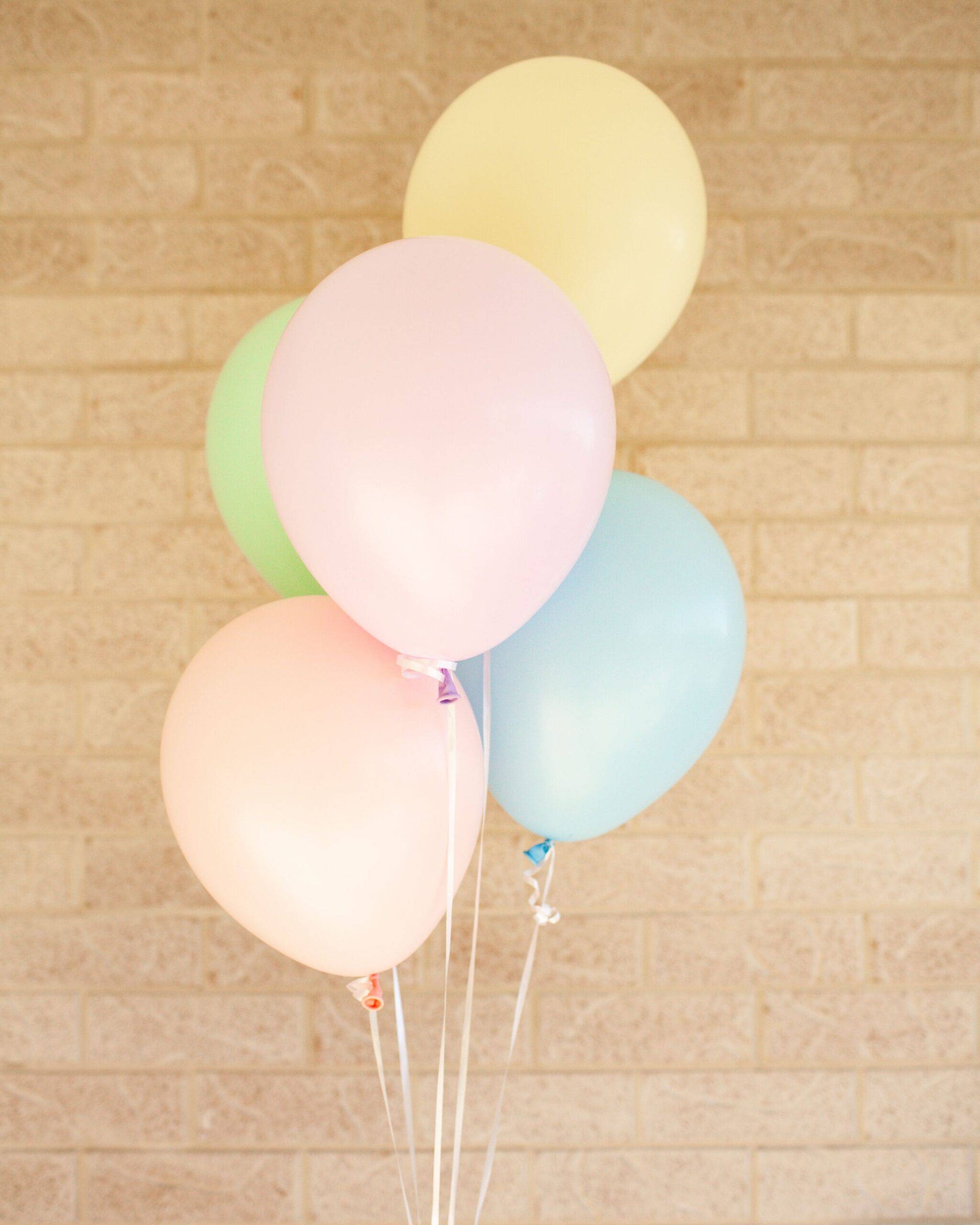 A cluster of pastel balloons in pink, green, yellow, and blue against a textured beige wall.